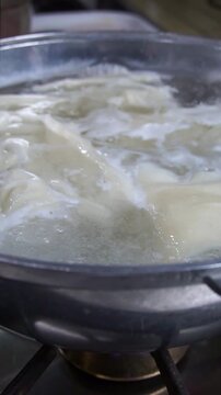 Close-up of fresh dough sheets boiling in hot water inside a metal pot for traditional beshbarmak