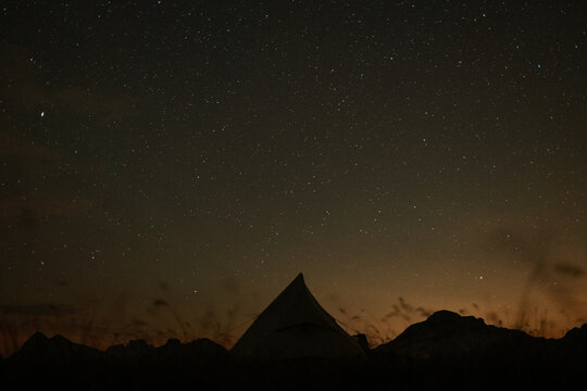 View of a tent silhouette set against the starry night sky with the peaks of Piz da Peres in the background in Mareo, Trentino-Alto Adige, Italy.