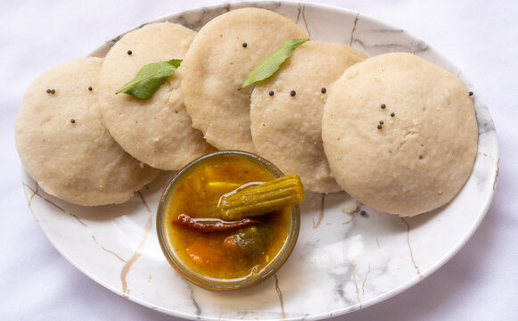 Side view of hot and steaming idly in a white plate and sambar in a isolated white background. Steaming hot idly served with sambar. Healthy food / Break fast in south India.