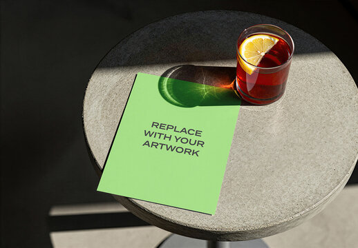 Square brochure mockup on a round concrete table with glass of red cocktail and lemon slice, realistic product presentation for print media, advertising display, editorial design