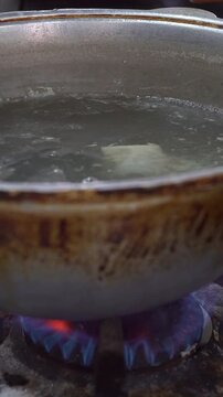 Chef putting fresh dough sheet into boiling water in a cauldron over gas stove burner