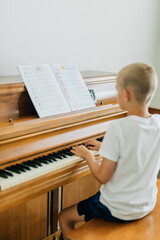 young boy sits at the piano playing sheet music © Jenisse
