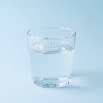 Verre d&rsquo;eau avec goutte cr&eacute;ant des ondulations sur fond bleu