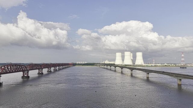 Slowly descending drone footage over the Padma River between Hardinge Bridge and Lalon Shah Bridge, showing Rooppur Nuclear Power Plant cooling towers and Green City Rooppur buildings.