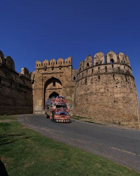 View of a colorful decorated truck passing through the historic stone gateway of Rohtas Fort in Dina, Punjab, Pakistan.