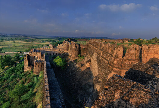 View of the historic stone walls and bastions of Rohtas Fort set against a lush green landscape under a clear blue sky in Dina, Punjab, Pakistan.