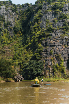 Small rowing boat on Tam Coc river beneath limestone cliffs