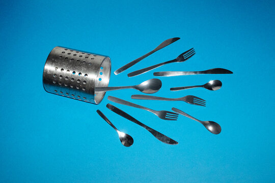 Metal cutlery spilling from utensil holder on blue background