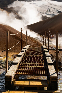 View of a metal footbridge leading into the geothermal landscape of Kerlingarfjoll with rising steam and volcanic hills in Hrunamannahreppur, Iceland.