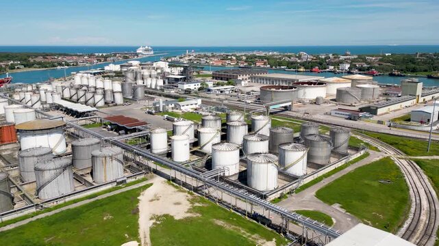 Aerial drone view of industrial chemical plant and oil storage tank farm in Ravenna port area with fuel silos pipes and cruise ship on horizon in Emilia Romagna Italy 