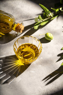 Olive oil in glass bowl with fresh branch and sunlight