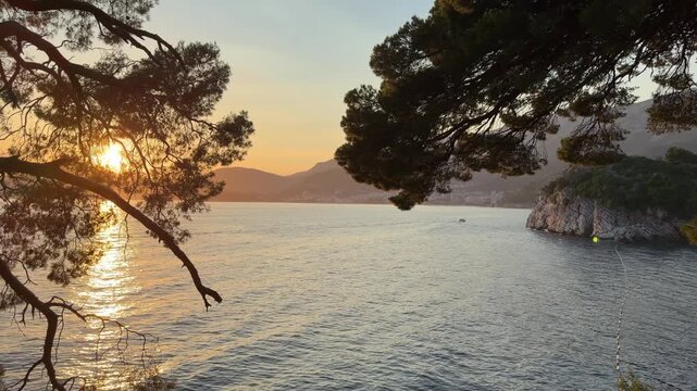 Sunset over a rocky seacoast, warm golden sunlight illuminating rugged cliffs and calm ocean waves in a peaceful summer landscape
