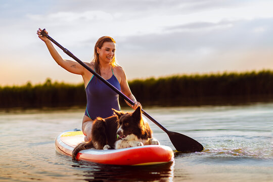 Active woman paddling on SUP board with her dog resting at front on lake.