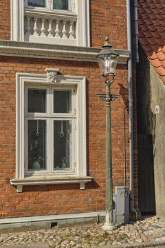 View of a vintage street lamp standing beside a historic red brick building with a white-framed window in the old town of Ribe, Denmark.
