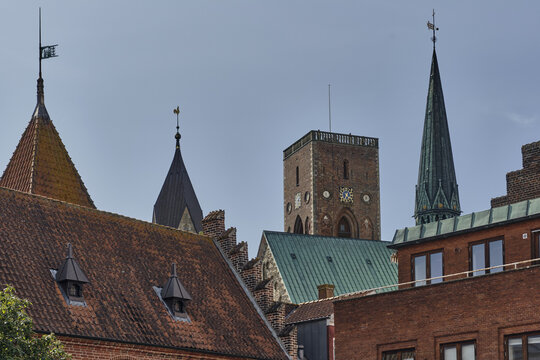 View of the historic Ribe Cathedral tower and spire rising above traditional red-tiled rooftops in the old town of Ribe, Denmark.
