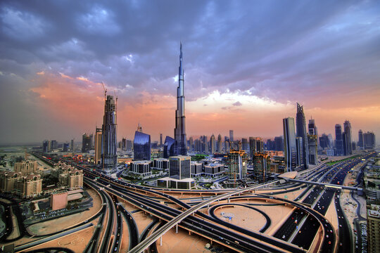 View of Burj Khalifa rising above the modern skyline and complex highway interchange during a vibrant sunset in Dubai, Dubai, United Arab Emirates.