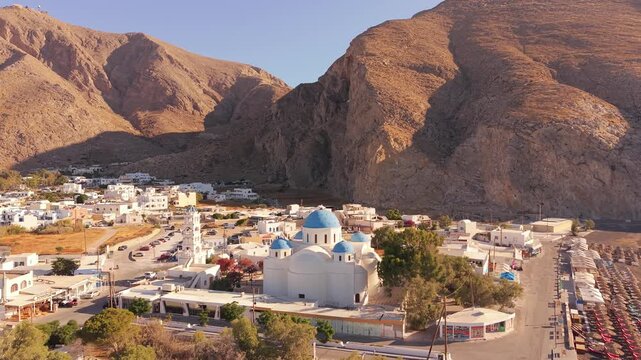 Drone view of Perissa Beach Kiosk blue dome church with Mesa Vouno mountain background Santorini Greece