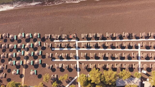 Top-down drone shot of symmetrical rows of straw umbrellas and sunbeds on Perissa black sand beach Santorini