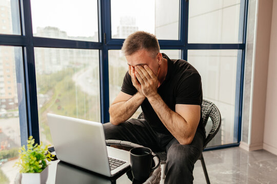 Stressed man with laptop during remote work on balcony
