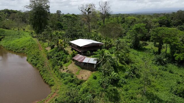 Drone Orbit of a Rustic Eco Lodge Finca in Costa Rica. traditional wooden farmhouse with a tin roof hidden in the lush green rainforest near pond.  Sustainable tropical living and eco tourism concept.