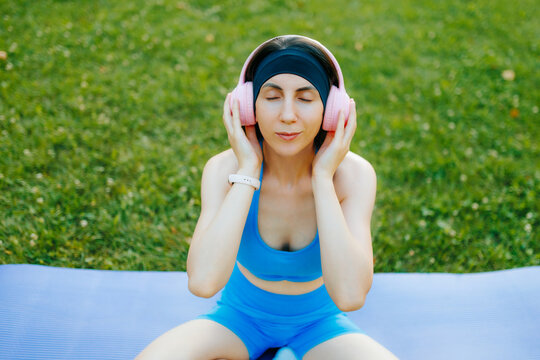Active fit woman listening to music on a yoga mat in the sunny park.