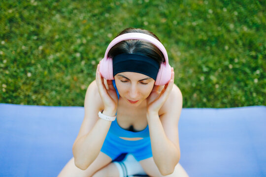 Top view of a fit woman enjoying relaxing music on the grass outdoors.