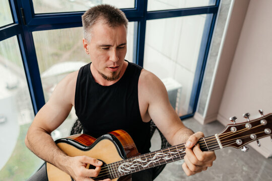 Man playing acoustic guitar on a glass balcony