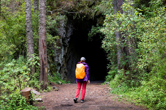 Hiker approach dark tunnel entrance in forest trail