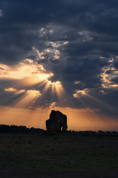 View of a 15th century tomb silhouette against a dramatic sunset with golden sun rays breaking through dark clouds in Bahawalnagar, Punjab, Pakistan.