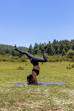 Woman practice yoga headstand in sunny mountain meadow