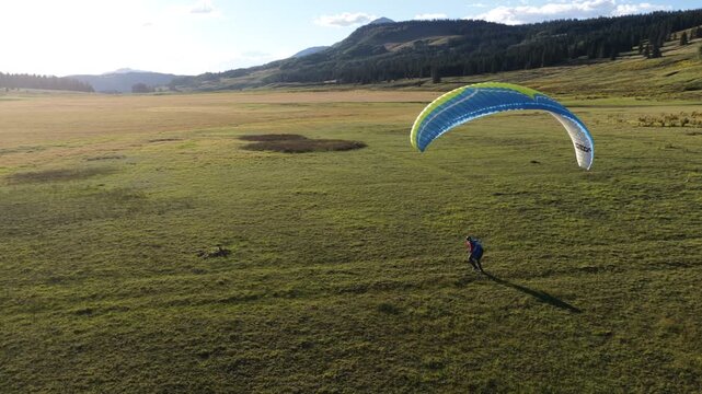 Aerial of person launching paraglider in San Juan National Forest Colorado with an arched blue kite wing at sunset in summer near Telluride