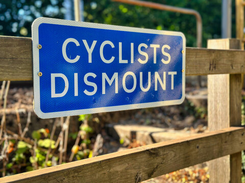 Blue "Cyclists Dismount" Information Sign on Wooden Fence outdoors
