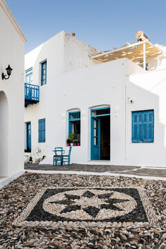 Traditional pebble mosaic pavement on a street in Plaka, Milos, surrounded by whitewashed Cycladic houses with blue doors and windows, Greece.