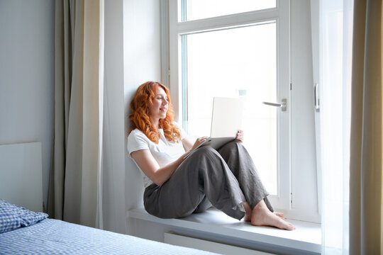 Redhead freelancer use laptop on bedroom windowsill at home