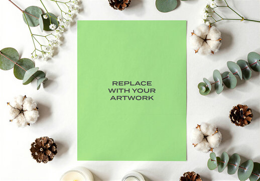 Vertical poster mockup on a white surface in natural flat lay arrangement with eucalyptus, cotton, pinecones, and baby's breath, minimalist interior display space for artwork