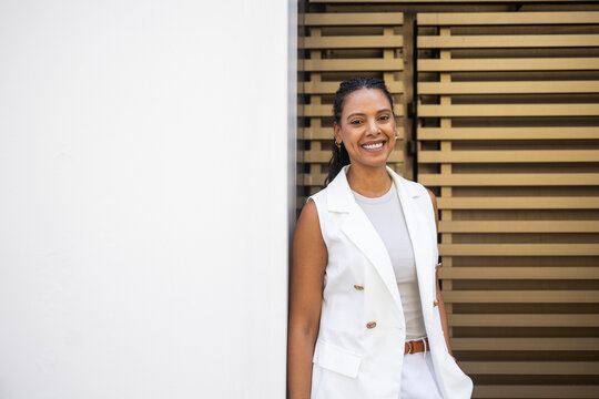 Smiling Hispanic businesswoman in white suit with braids