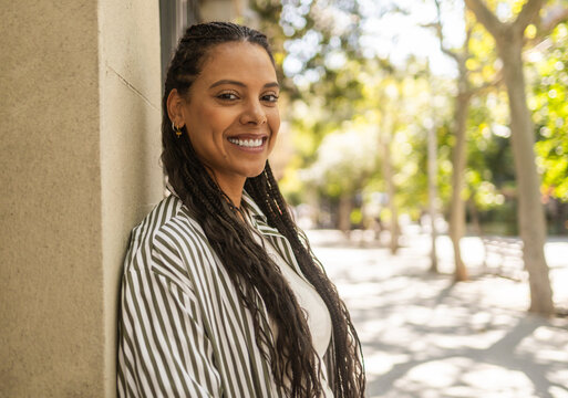 Smiling Hispanic woman with braids outdoors in sunlight
