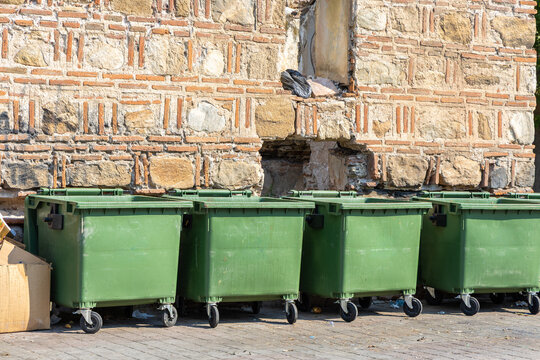 View of green plastic waste bins lined up against a historic stone and brick wall in Prilep, Prilep Municipality, North Macedonia.