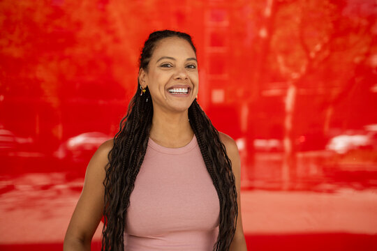 Smiling Hispanic woman with braids against red background