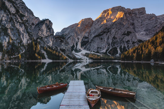 View of wooden rowboats at a pier on the calm, reflective waters of Lago di Braies in the Dolomites, surrounded by towering limestone peaks, Campitello di Fassa, Trentino-Alto Adige, Italy.