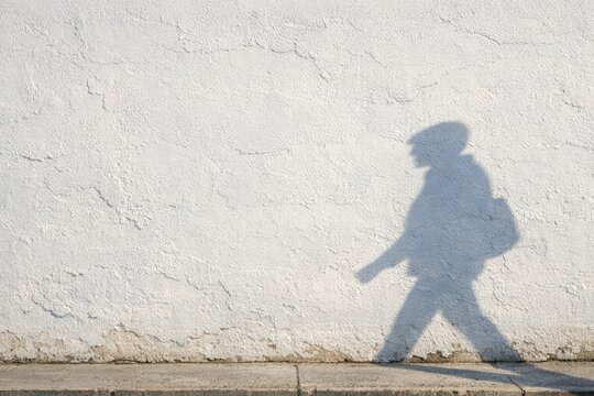 A person is walking alone on a city sidewalk at night, with a faint shadow visible