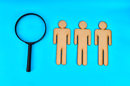 Magnifying glass beside three wooden people for recruitment and talent search on turquoise background

