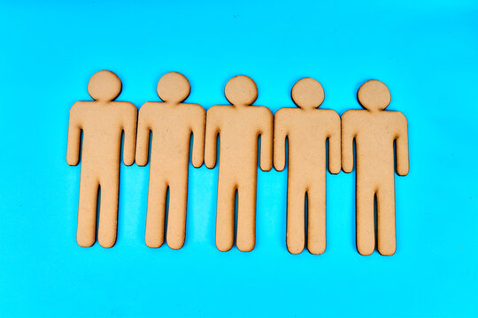 Five wooden human figures standing together as a team on turquoise background
