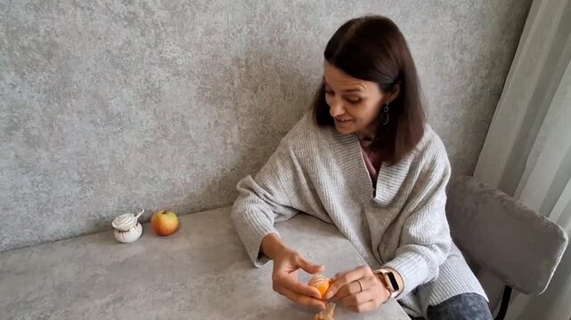 Woman peeling an orange at a table in a cozy kitchen in the morning