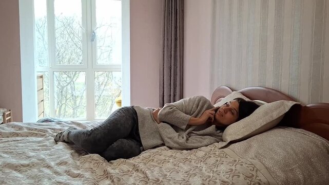 Woman resting on bed in cozy room with window during a quiet morning
