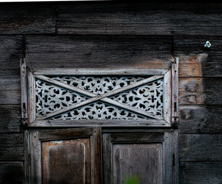 Carved Wooden Cross Pattern Transom Window on Dark Wooden Wall, Traditional Thai House Detail