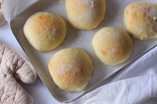 Freshly baked ciabatta bread rolls displayed on a metal baking tray lined with parchment paper. Soft texture, golden crust, and a minimalist homemade presentation create an inviting bakery scene