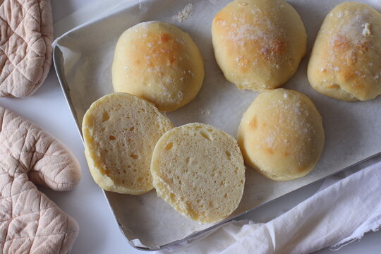 Homemade ciabatta bread rolls arranged on a parchment-lined baking tray with sliced pieces revealing the soft, airy crumb. Rustic food styling highlights texture, freshness, and artisan baking