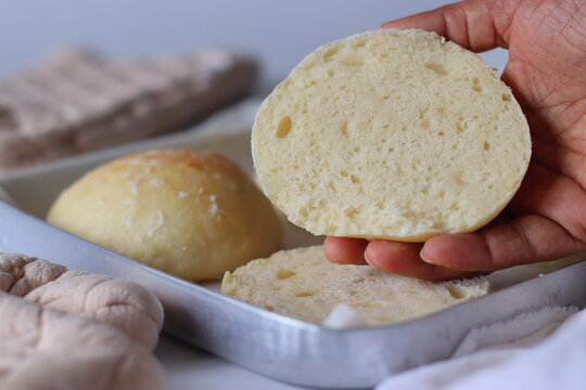 Close up of a freshly baked ciabatta bread roll with a hand holding the sliced piece to reveal its soft, airy interior. Rustic food styling highlights homemade baking and bread texture