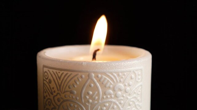 Candle burning glowing flame close up ornate white wax against black background